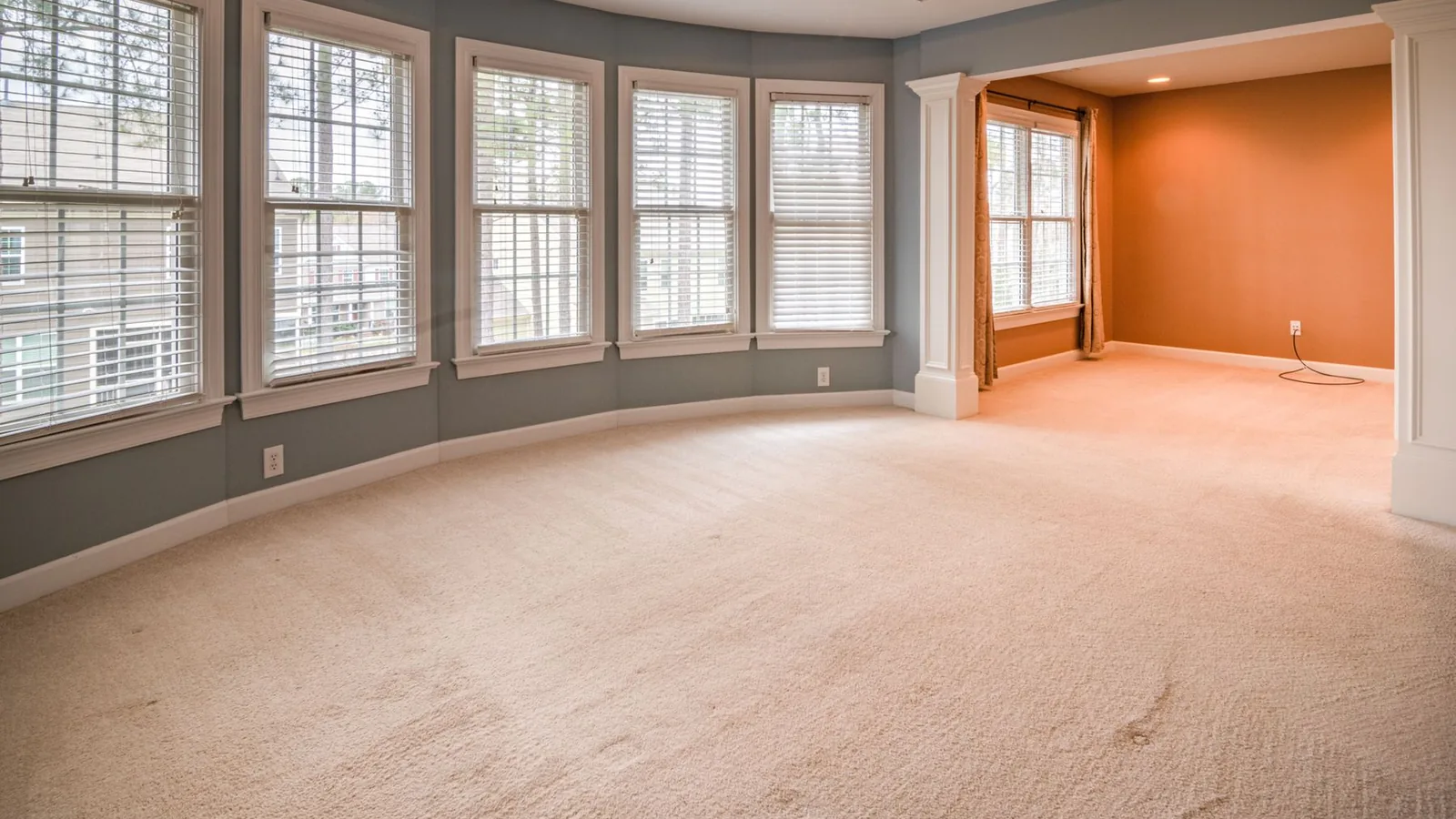 Bright empty room with new carpet, large windows and an orange accent wall